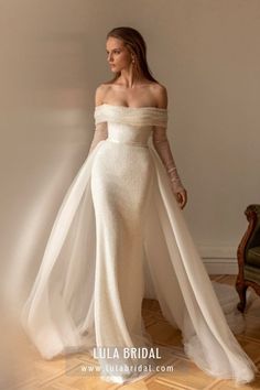 a woman in a white dress standing on a wooden floor wearing an off - the - shoulder gown