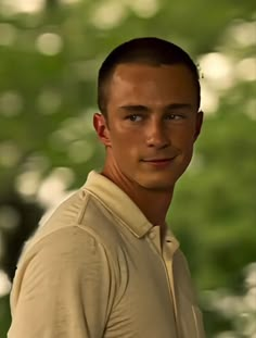 a young man is posing for a photo in front of some trees and grass with his head tilted to the side