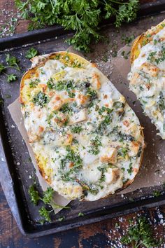 two baked potatoes covered in cheese and herbs on a baking sheet next to parsley