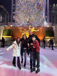 three people standing on an ice rink in front of a large christmas tree with lights