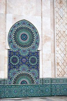 an intricately designed wall with blue and green tiles on the outside, in front of a white building