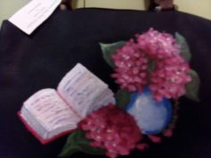 a blue vase filled with pink flowers next to an open book on a black chair