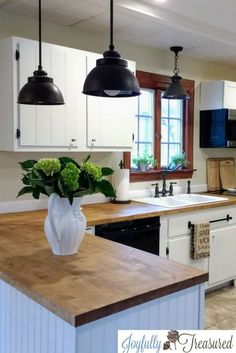 a kitchen with white cabinets and wooden counter tops, black pendant lights over the sink