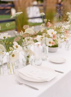 the table is set with white and pink flowers in glass vases, plates and silverware