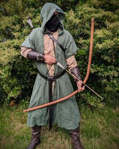 a man dressed in medieval clothing holding a bow and arrow while standing on the grass