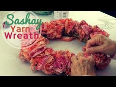 a person making a wreath out of yarn on top of a white table with the words sashay yarn wreath above it