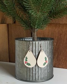 a small christmas tree in a tin can with two earrings hanging from it's side