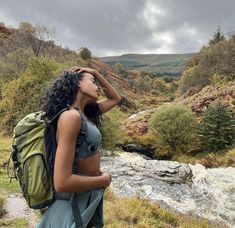 a woman standing in front of a river with a backpack on her back and looking into the distance