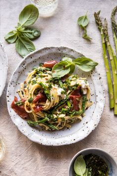 a white plate topped with pasta and veggies next to green asparagus