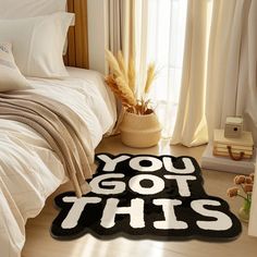 a bed room with a neatly made bed and a rug that says you got this