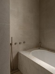 a bath tub sitting next to a shower head in a bathroom with marble walls and floor