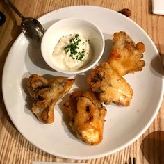 a white plate topped with fried food next to a bowl of ranch dressing on top of a wooden table