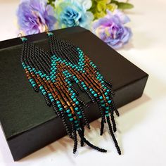 the beaded necklace is on display in front of some purple and blue flowers next to a black box