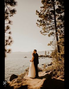 a bride and groom are standing on the rocks by the water