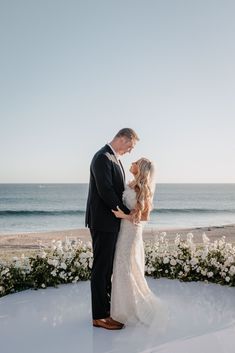 a bride and groom standing in front of the ocean