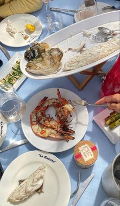 people sitting at a table with plates and food on it, including lobsters, as well as wine glasses