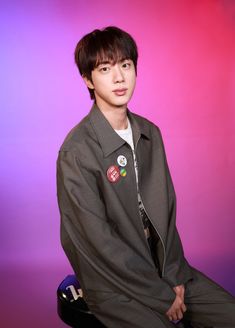 a young man sitting on top of a chair wearing a jacket and tie with buttons