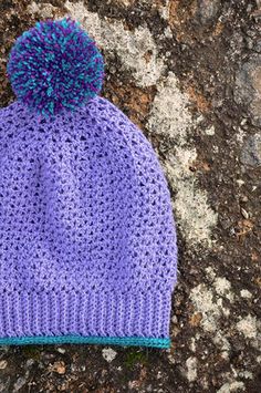 a purple hat with a blue pom - pom sits on top of a rock