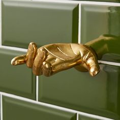 a gold hand holding onto a green tiled wall