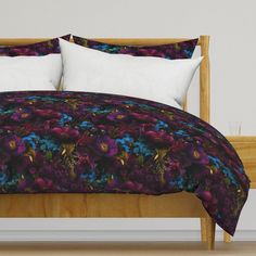 a bed with purple and blue flowers on the comforter is in front of a white wall