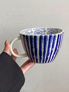 a hand holding a blue and white striped coffee cup in it's right hand