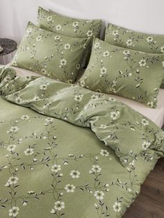 a bed with green sheets and white flowers on the comforter, along with two pillows