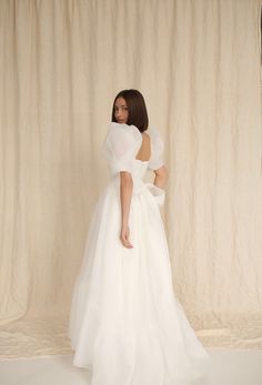 a woman in a white dress standing against a curtain with her back to the camera