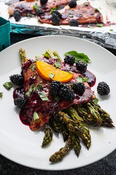 a white plate topped with asparagus, orange slices and blackberry topping on top of it