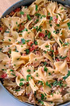 a skillet filled with pasta and meat covered in parsley on top of a table