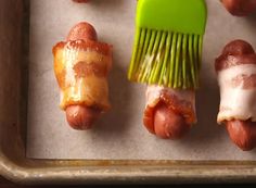 bacon wrapped hot dogs on a baking sheet with a green brush