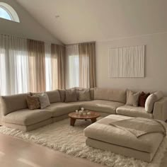 a living room with a large sectional couch and coffee table in front of two windows