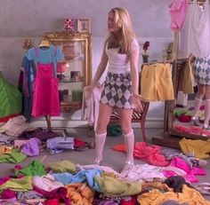 a woman standing in front of a pile of clothes on the floor next to a mirror