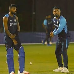 two men standing next to each other on top of a field holding cricket balls in their hands