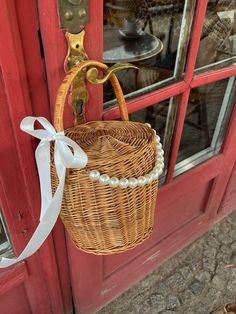 a wicker basket hanging on a red door with a white ribbon attached to it