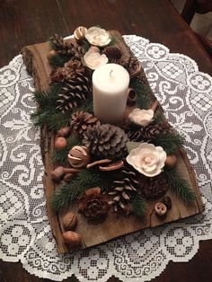 a wooden tray with pine cones, candles and flowers sitting on top of a doily