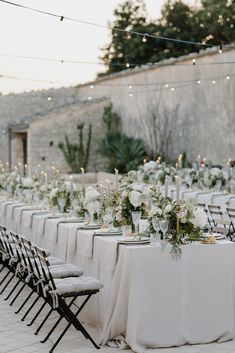 a long table with white flowers and greenery is set up for an outdoor dinner