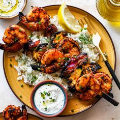 grilled shrimp and rice on a plate with lemon wedges next to dipping sauce