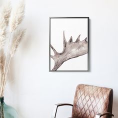 a chair sitting next to a vase with flowers in it and a painting on the wall