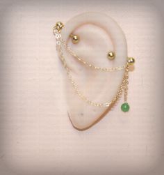 a pair of ear rings with pearls and green beads on them sitting on top of a white surface