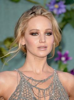 a close up of a person wearing a dress and eyeliner with flowers in the background