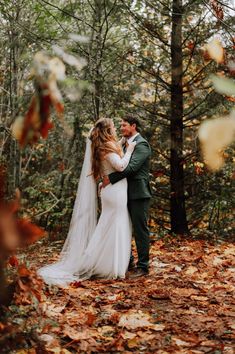 a bride and groom standing in the woods surrounded by fallen leaves on their wedding day