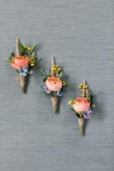 three boutonnieres with flowers and greenery are arranged on a gray surface