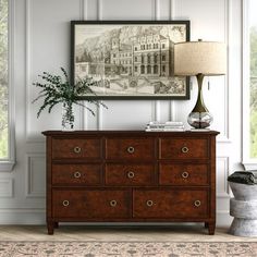 a room with a dresser, lamp and pictures on the wall