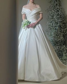 a woman in a white wedding dress standing next to a wall with flowers on it