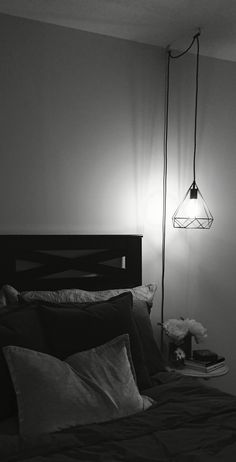 a black and white photo of a bed in a room with a lamp on the wall