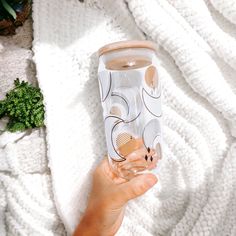 a person holding up a glass on top of a white blanket next to a potted plant