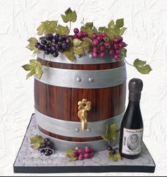 a wine barrel cake with grapes on top and a bottle of wine next to it