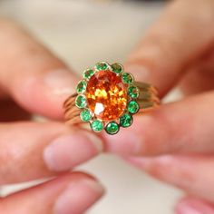 a woman is holding an orange ring with green stones