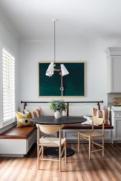 a dining room table with two chairs and a bench in front of a painting on the wall