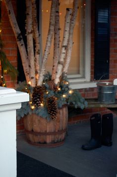 a potted plant with pine cones and lights in it on the front porch next to a white fence